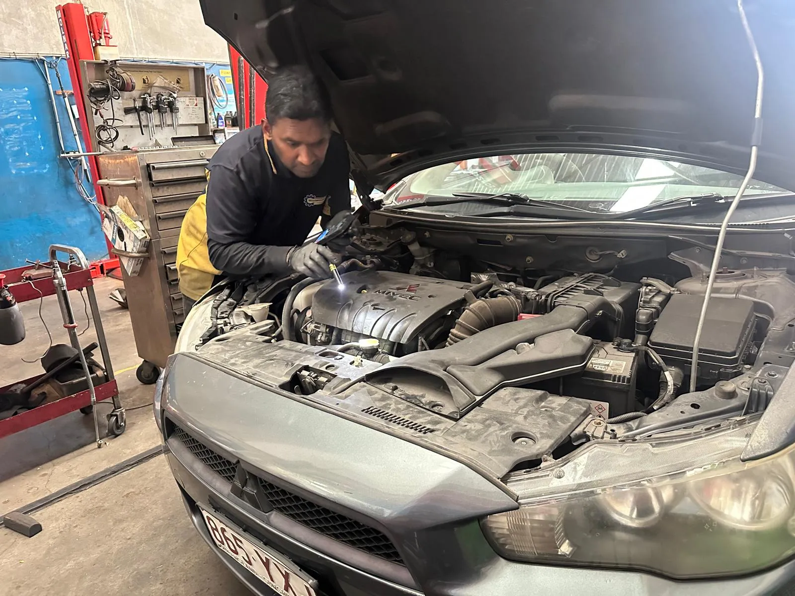 SRID technician inspecting an engine bay with a torch